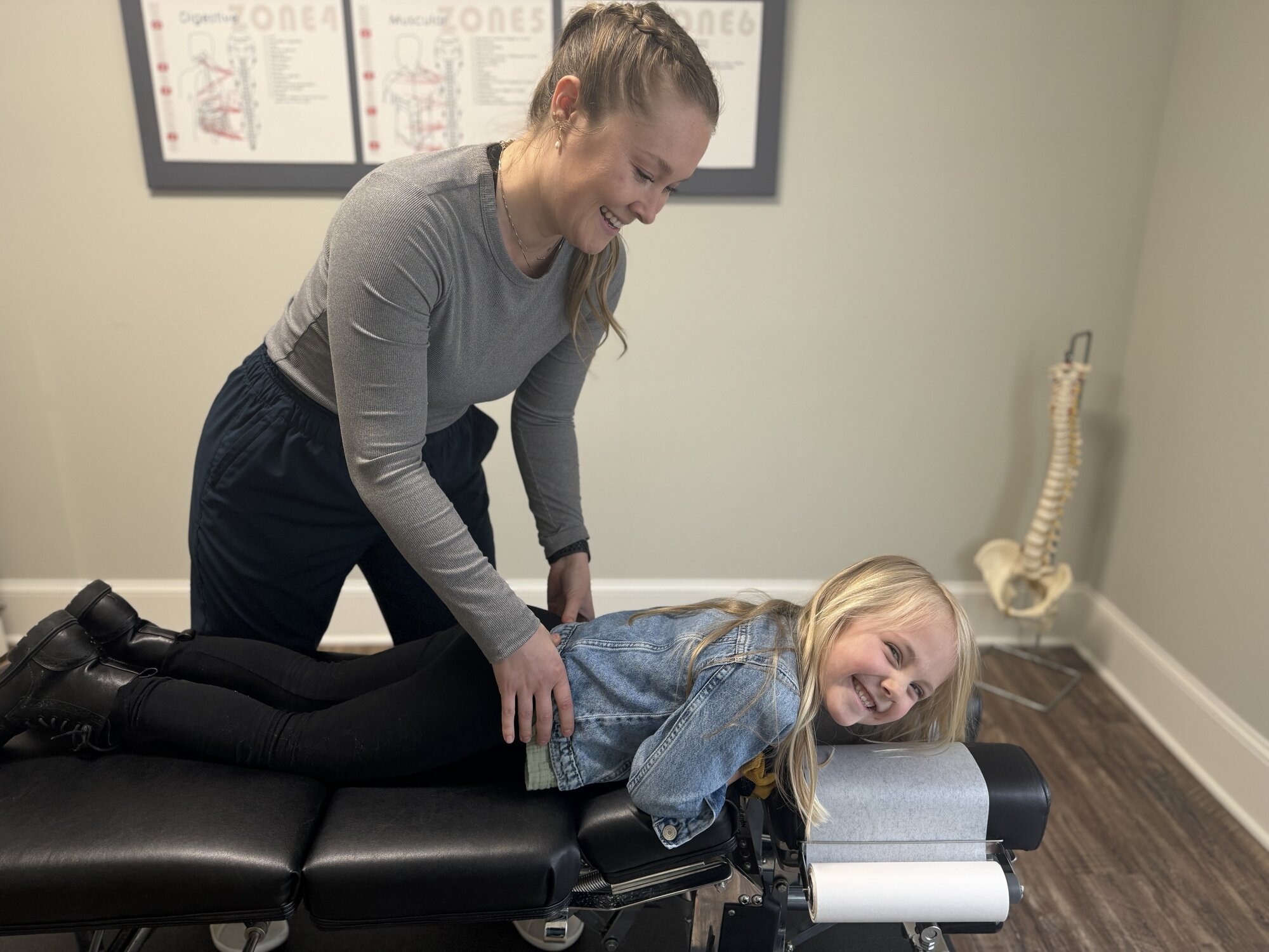 Dr. Corie Terwilliger smiling during a pediatric adjustment as her young patient grins at the camera in the treatment room