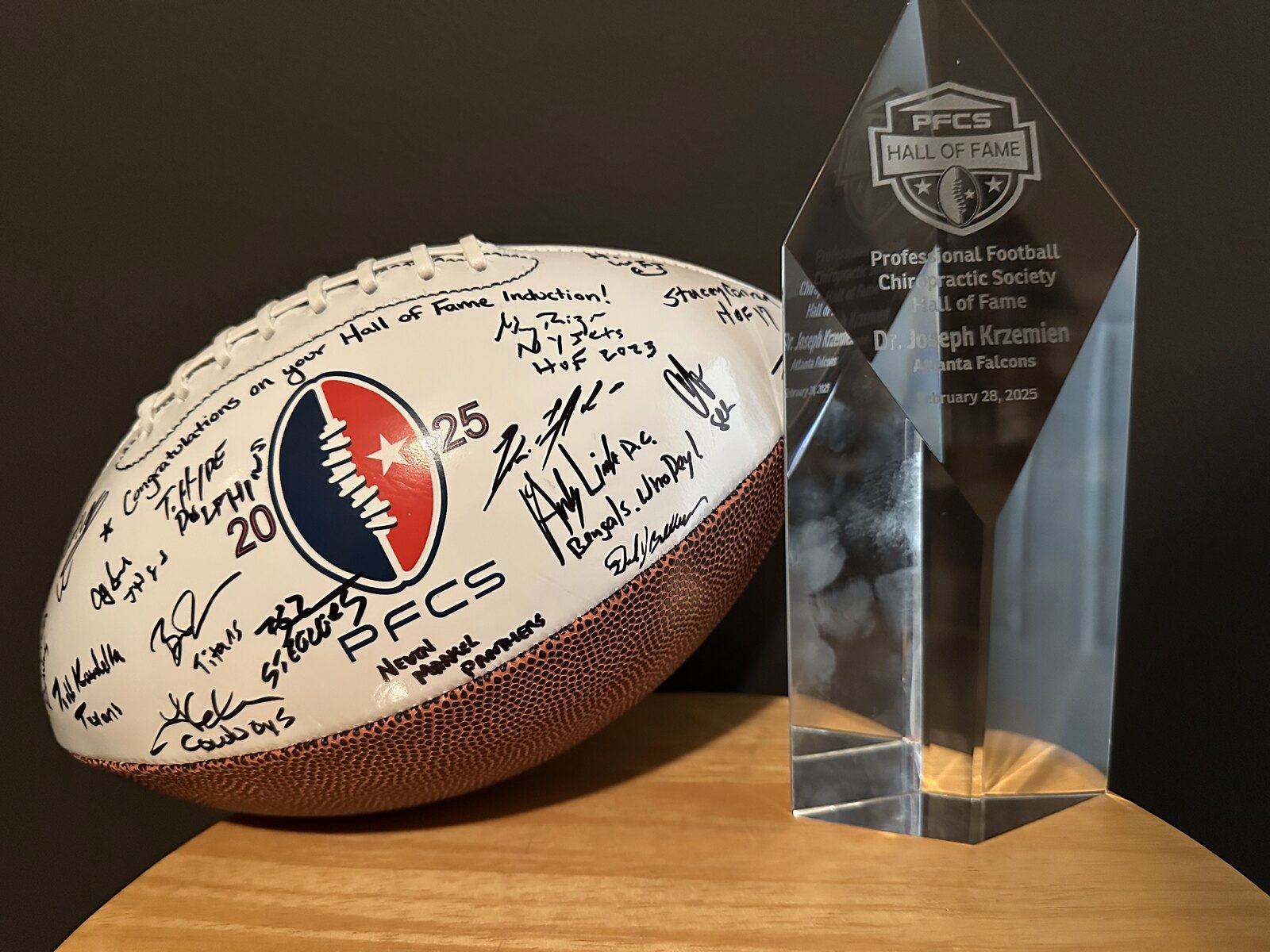 The PFCS Hall of Fame crystal trophy engraved 'Dr. Joseph Krzemien, Atlanta Falcons, February 28, 2025' next to the signed Class of 2025 induction football