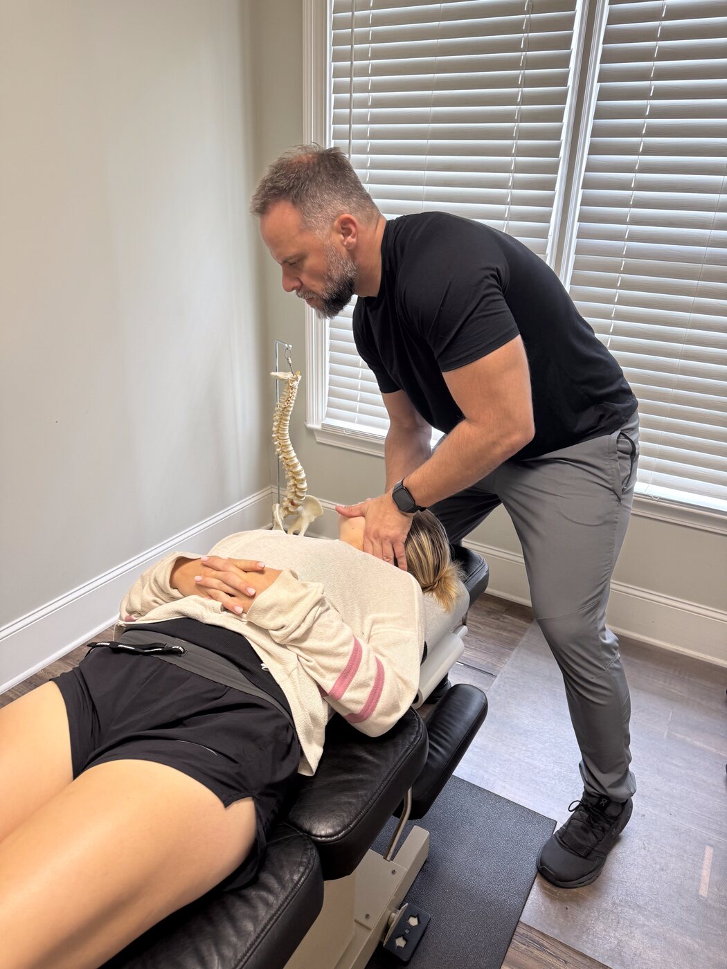 Dr. Joe Krzemien performing a low-back adjustment on a patient at Georgia Spine and Sports Rehab, with a spinal anatomy model visible in the treatment room