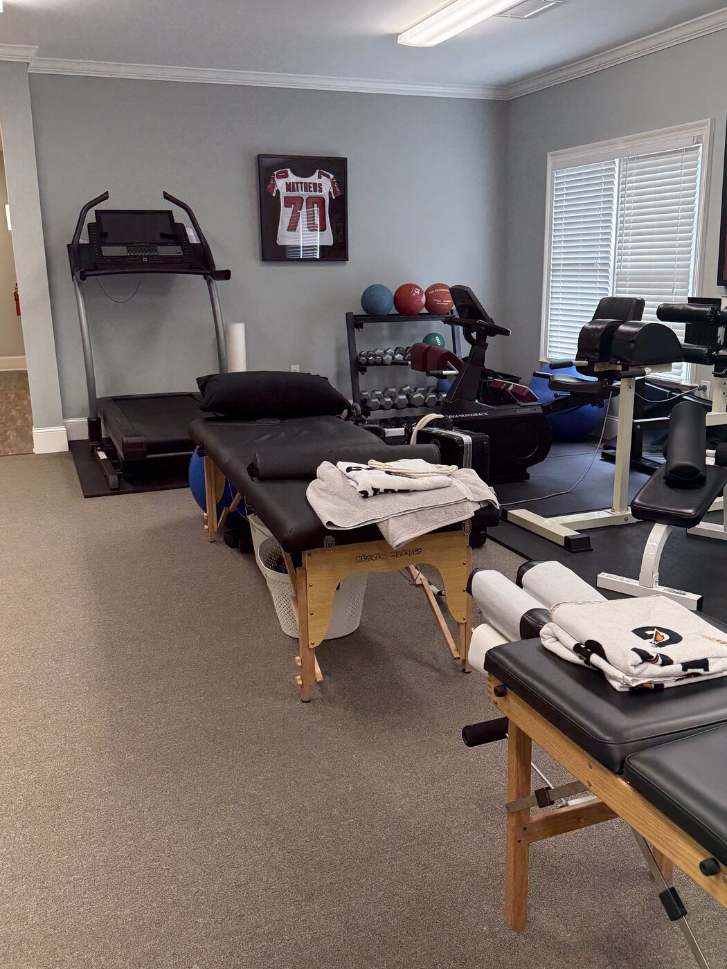 A second view of the rehab gym showing a treadmill, free-weight stack, ARP wave unit, and Jake Matthews #70 Atlanta Falcons jersey framed on the wall