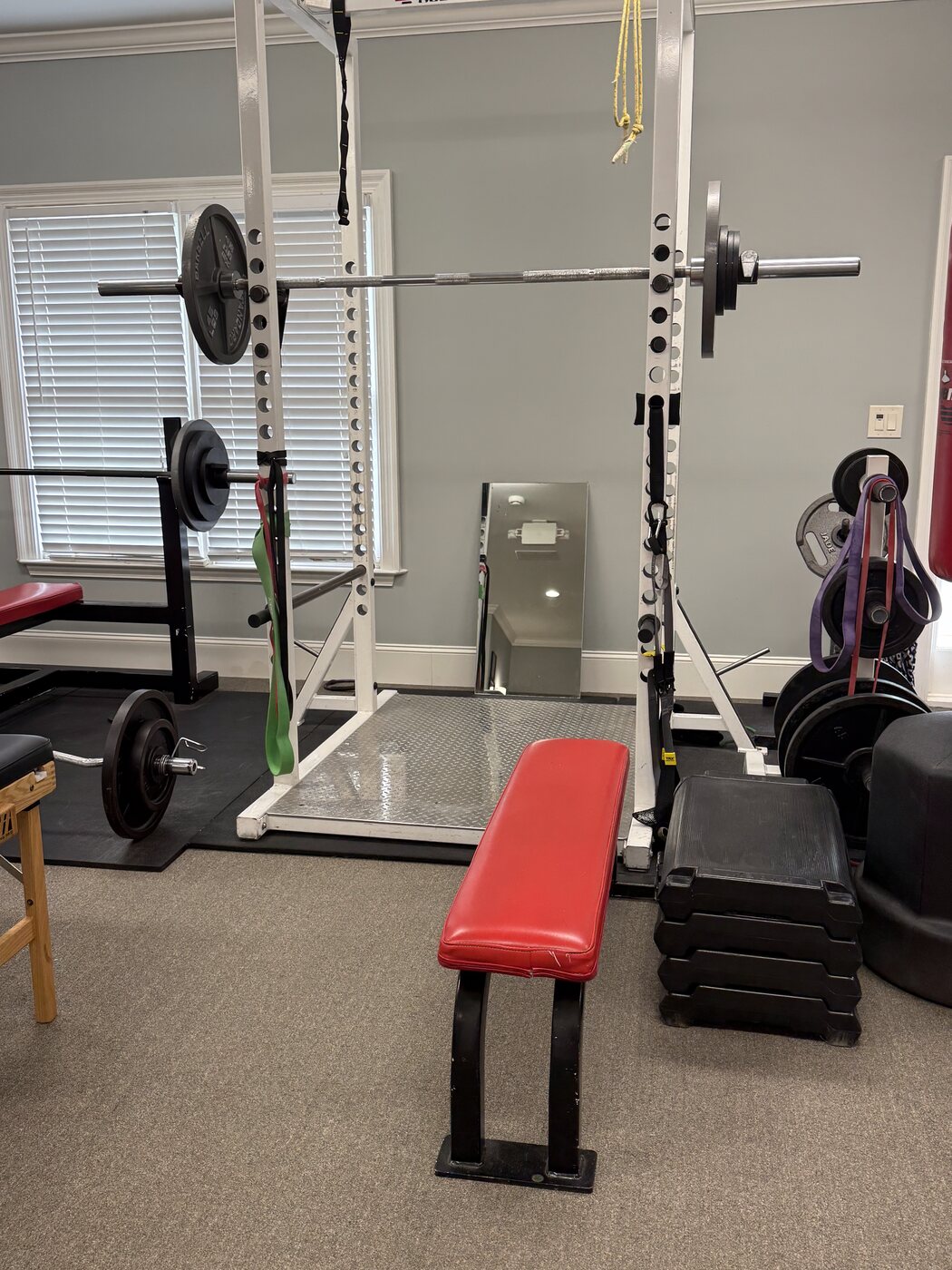 Closeup of the power rack and bench press setup in the rehab gym, with weight plates, barbell, and step boxes