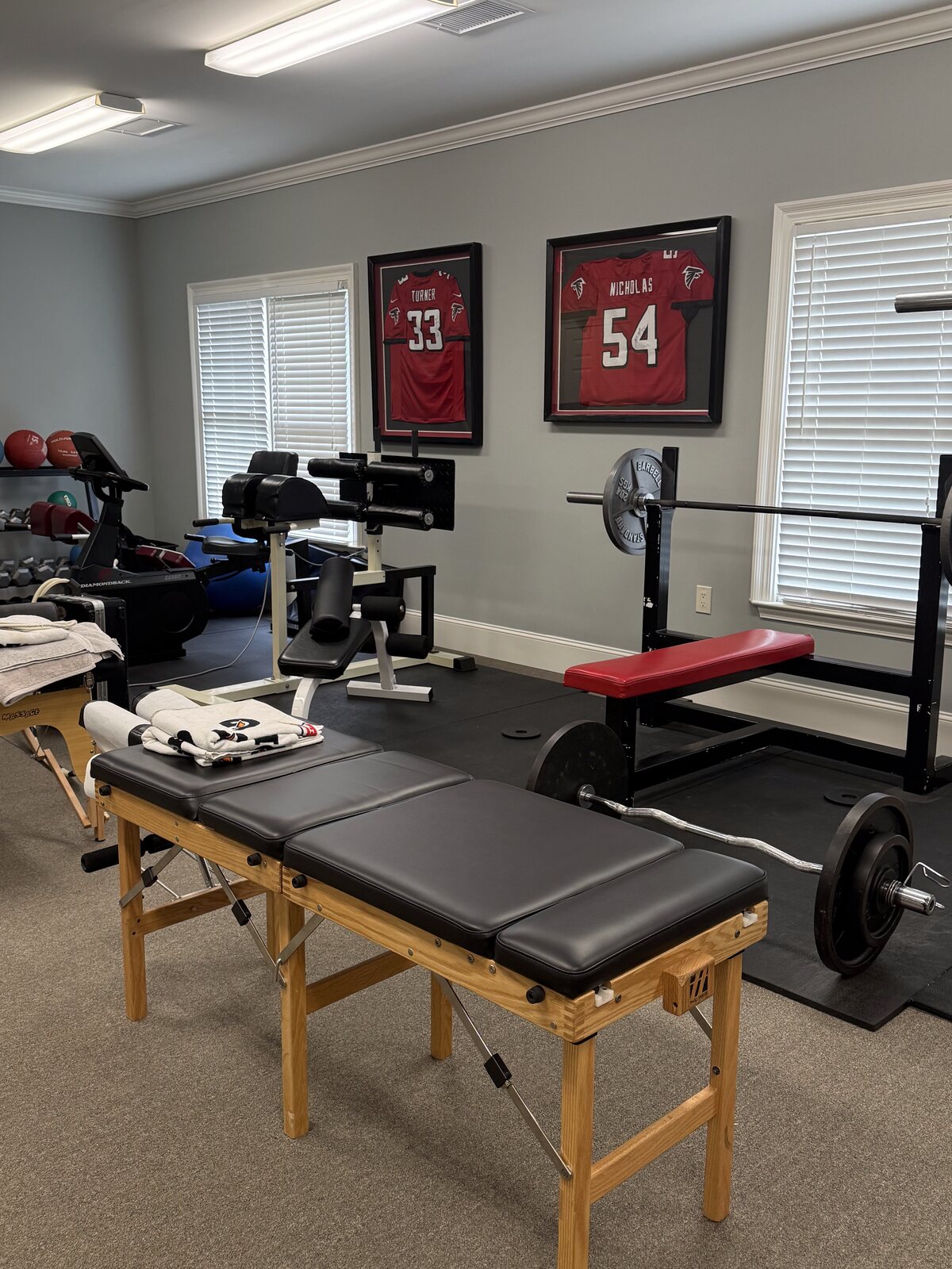 The rehab gym at Georgia Spine and Sports Rehab, with three framed Atlanta Falcons player jerseys on the wall above a power rack and bench press setup