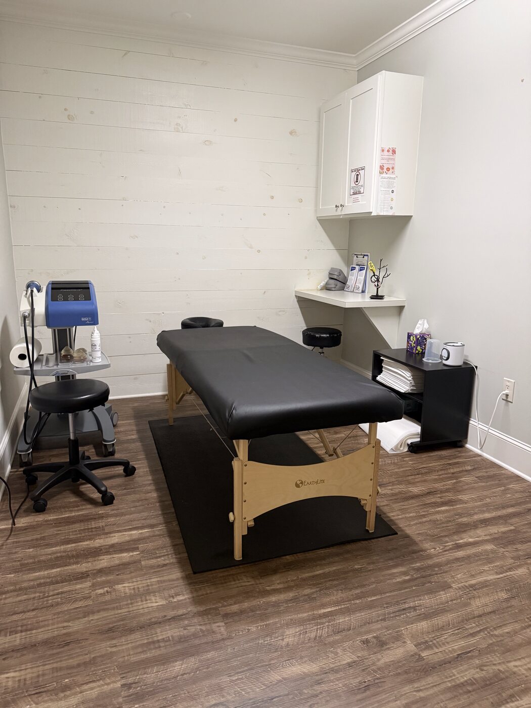 A second treatment room at Georgia Spine and Sports Rehab with a white shiplap accent wall, a portable adjustment table, and ARP wave electrical stimulation unit